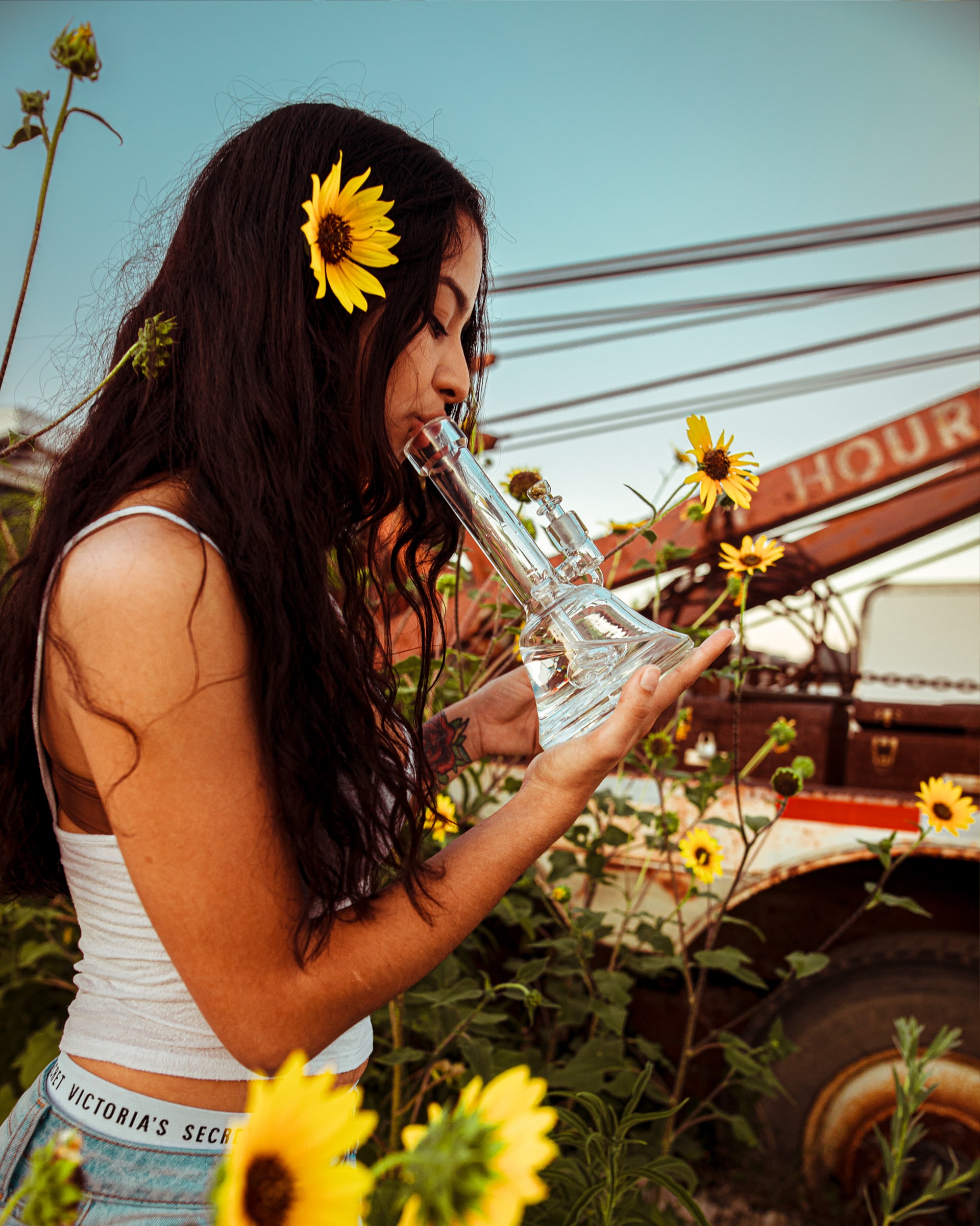 A woman holds a water pipe to her lips while standing in yellow flowers