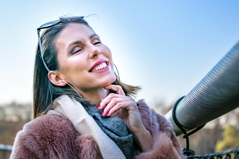 Smiling happy woman with eyes closed standing on a bridge