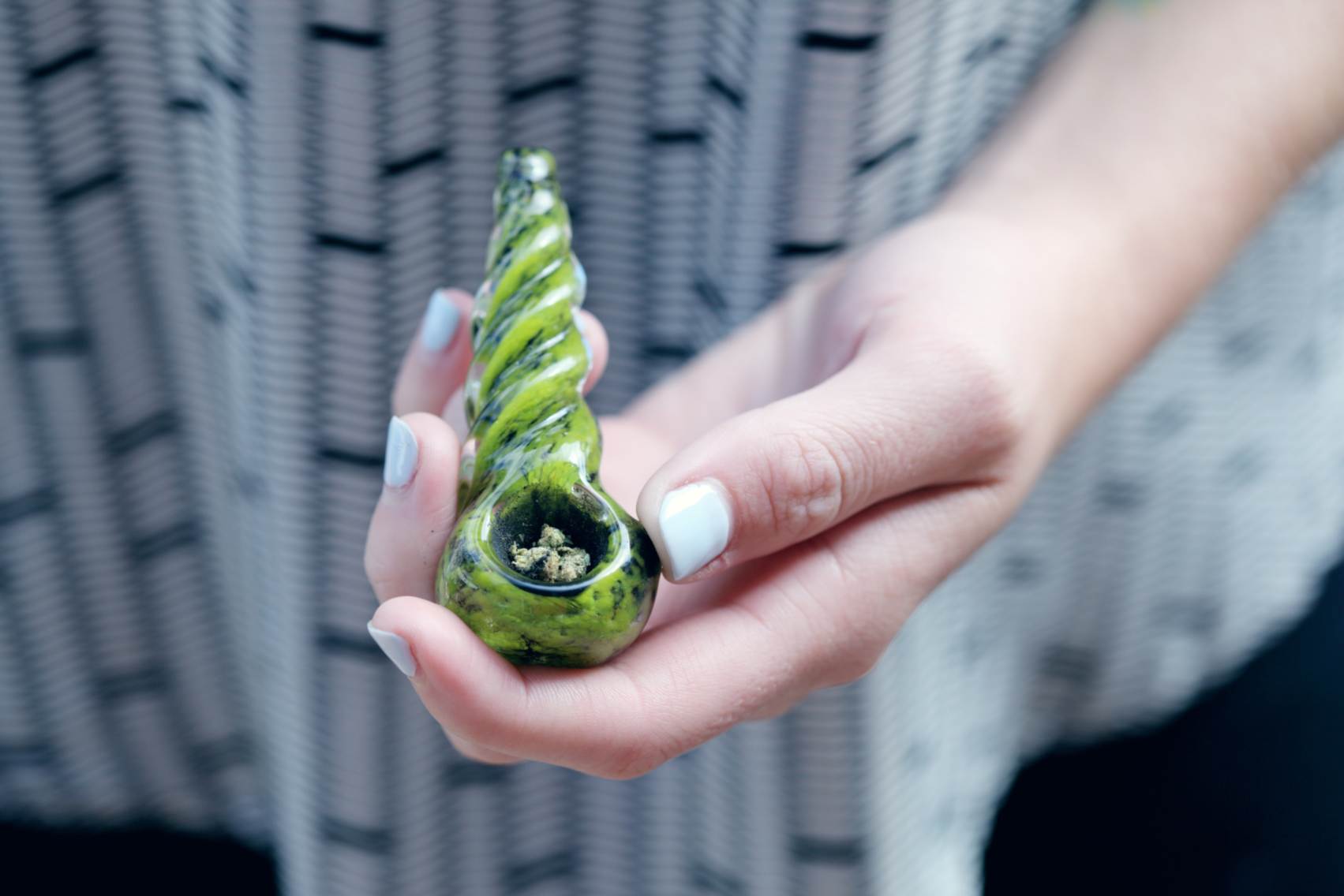 Close-up of a person holding a green glass pipe with medical marijuana in it