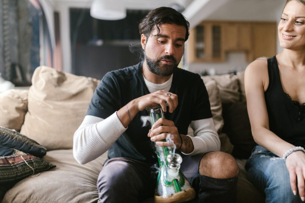 A man sitting next to a woman and holding a bong