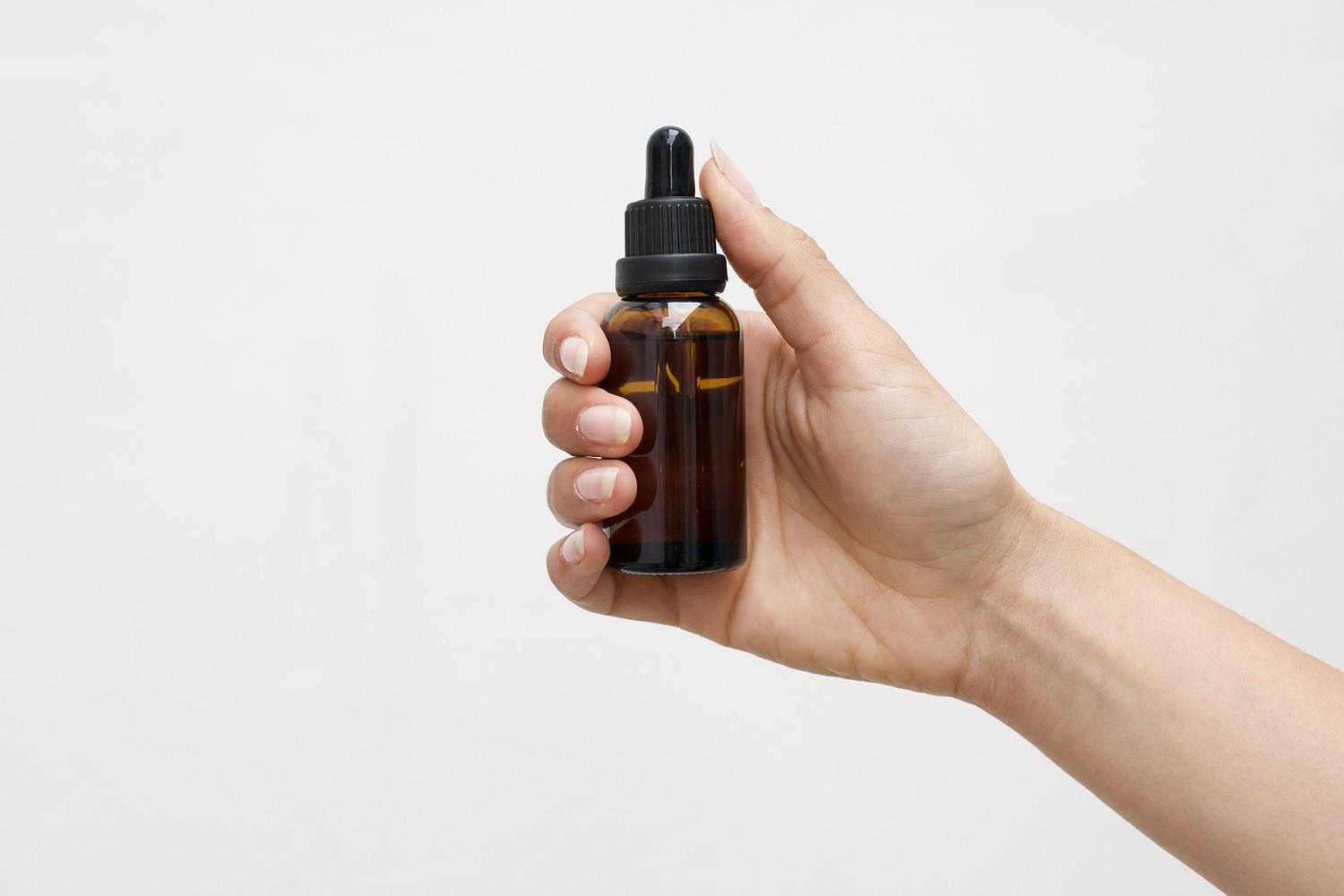 Hand holding cannabis tincture bottle against a white background